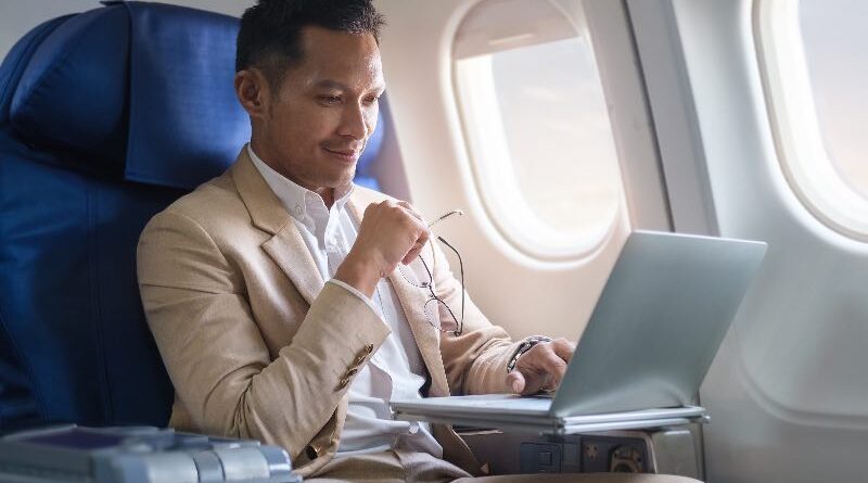 Elegant businessman using laptop while sitting in airplane cabin with sun shining trough airplane window.