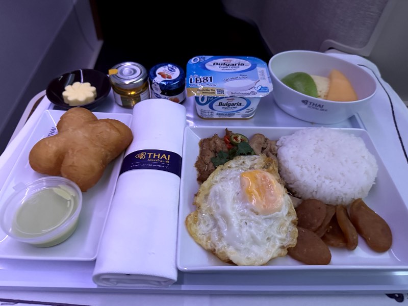 Thai Airways Business Class breakfast including seasonal fruits, yoghurt, patongko, and chicken with mushrooms and bamboo shoots in gravy served with Thai jasmine rice, Chinese chicken sausages and fried egg