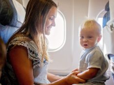 Young mom, playing with her toddler boy on board of aircraft, going on holiday