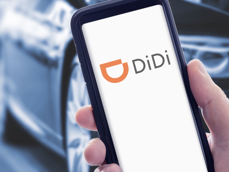 Hand holding a smart phone with DIDI logo on screen and car in background