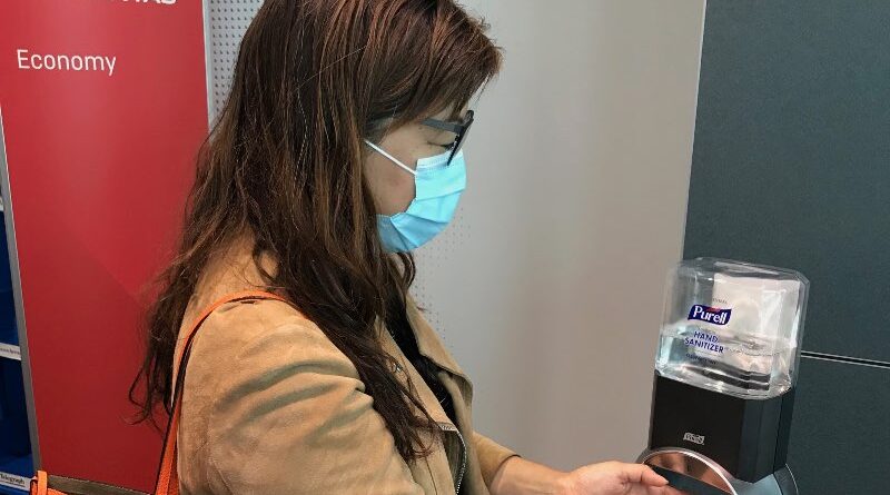 Passenger wearing face mask uses hand sanitiser at Qantas boarding gate